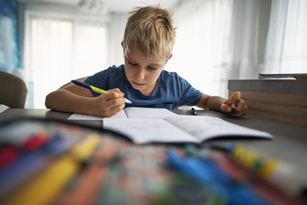 Young boy in blue shirt doing homework at the kitchen table.
