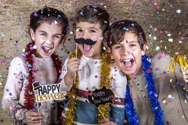 Two boys and a girl covered in confetti and holding Happy New Year signs.