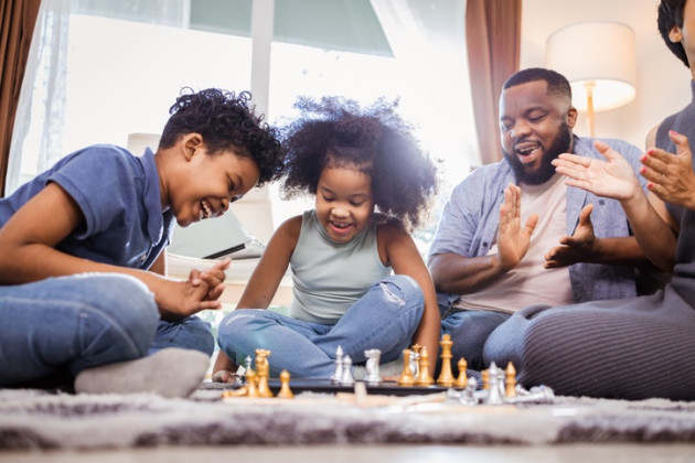Family playing chess on the floor of their family room for family game night.